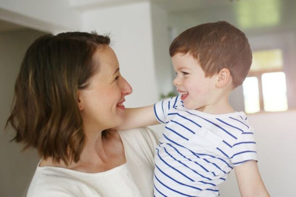 A woman smiles at her toddler as she holds him