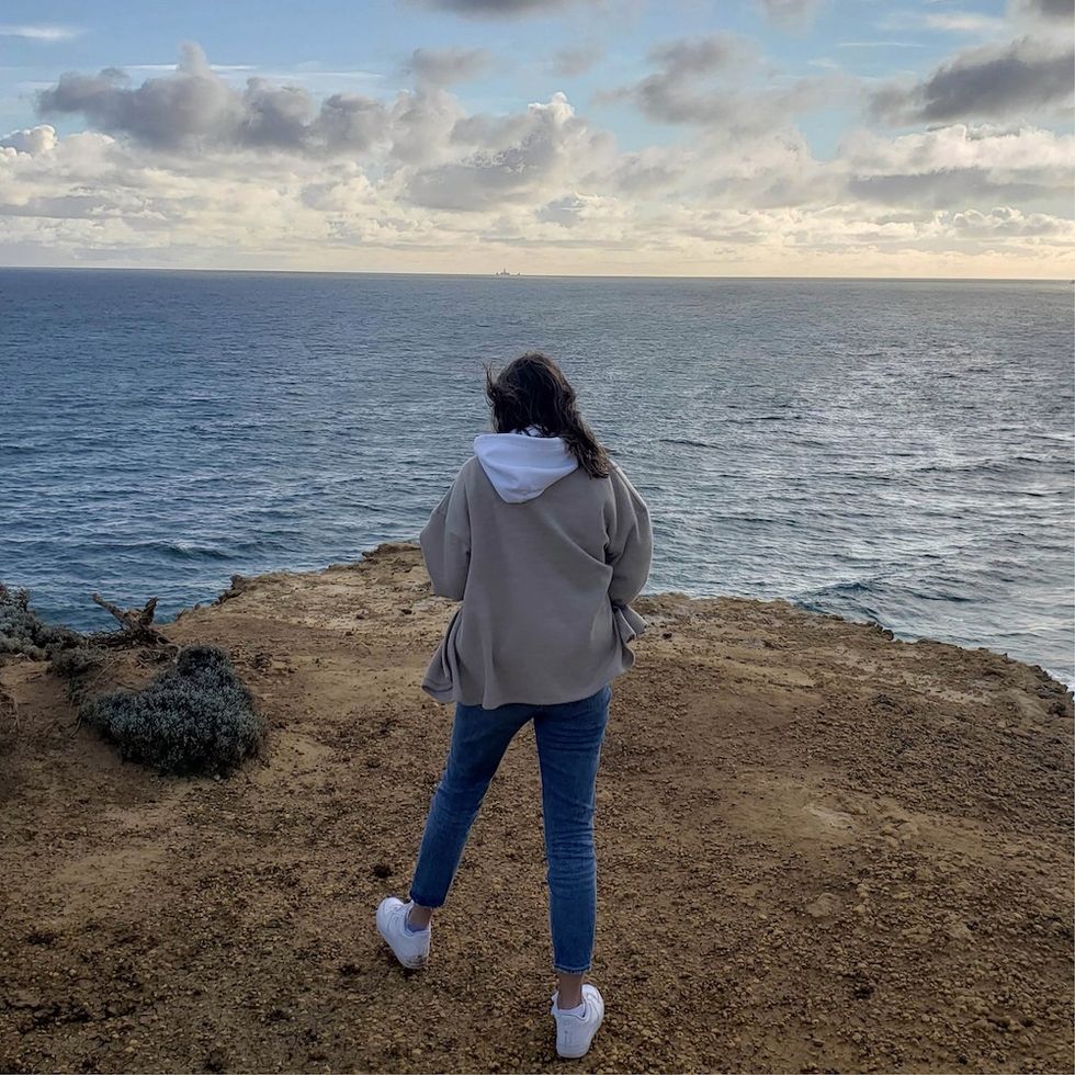 a woman standing in front of the water, looking out into the distance