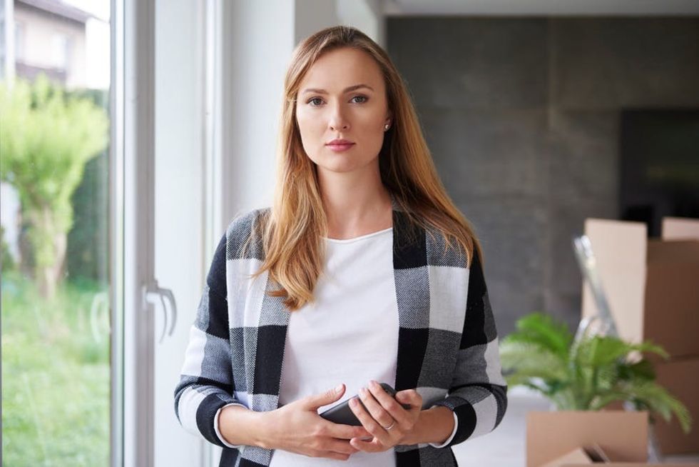 A woman stands in a sunny room with several packed boxes in the background