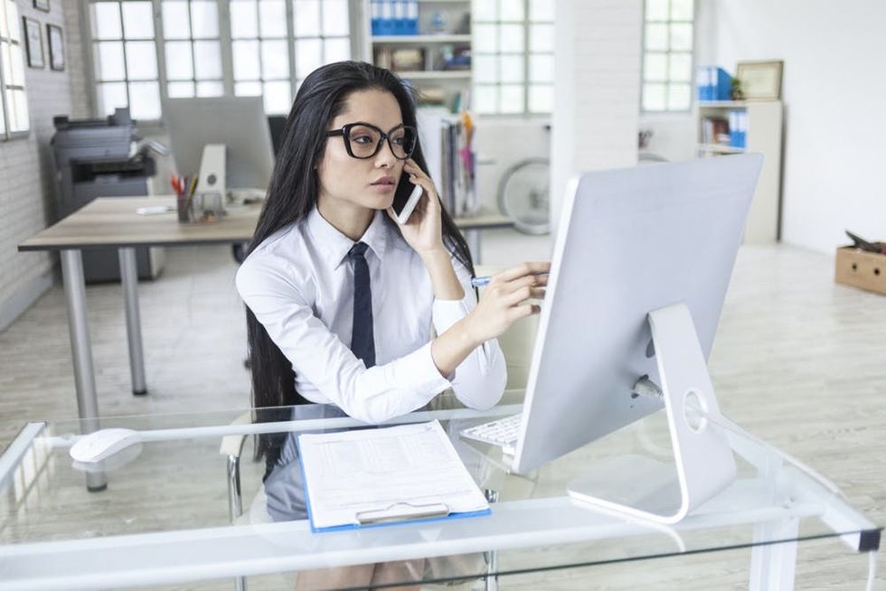A woman talks on the phone while pointing at her computer monitor