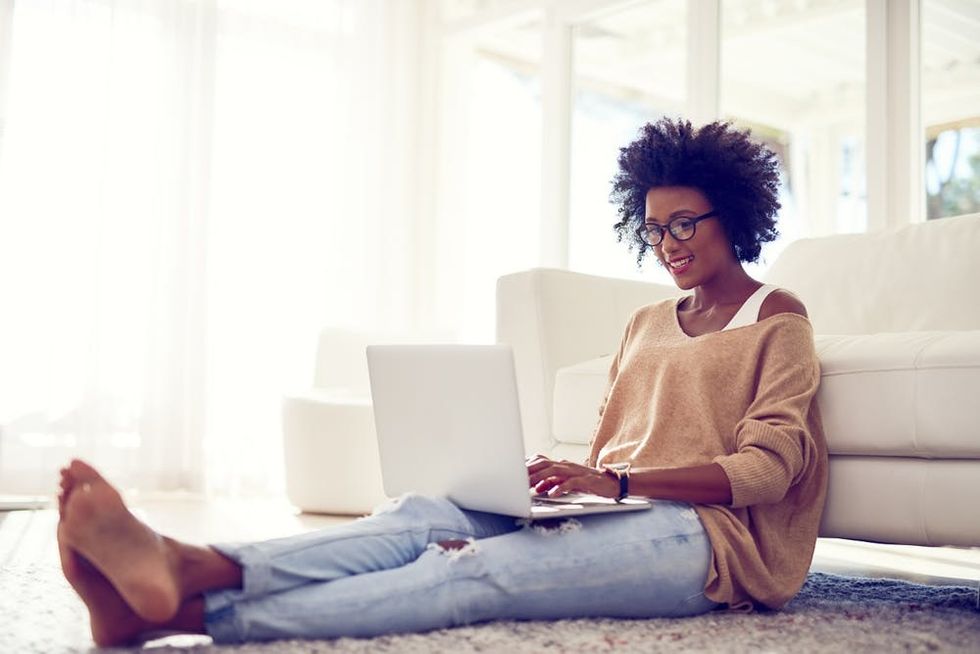 A woman uses a laptop as she sits in front of her couch