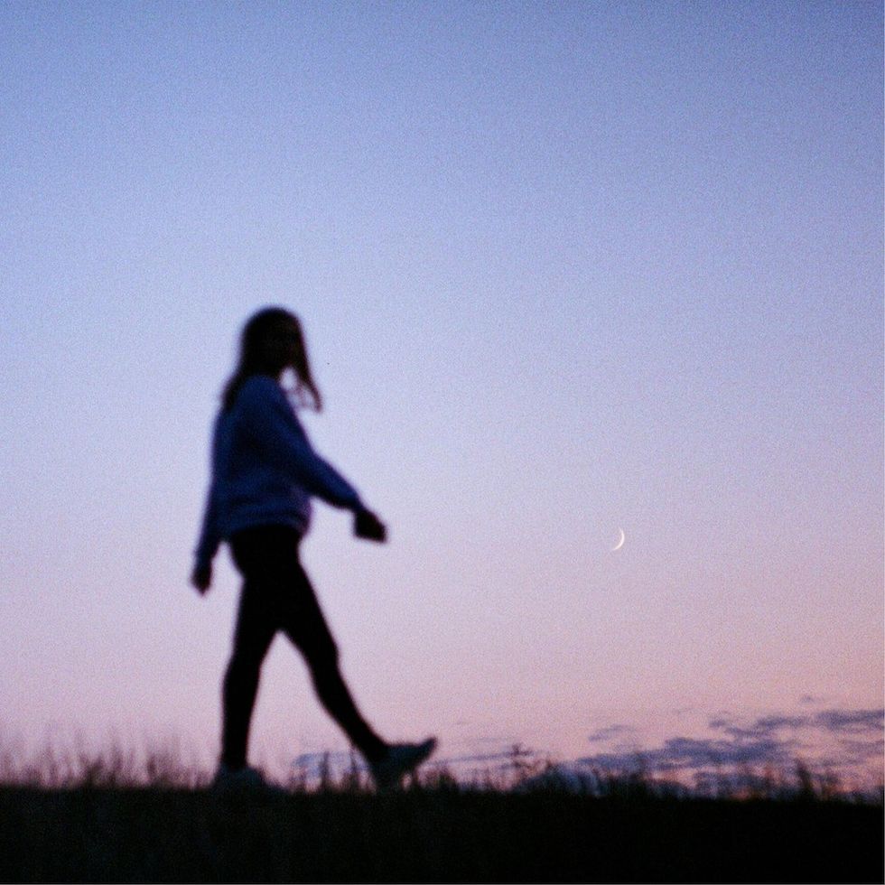 a woman walking at sunset with the crescent moon behind her