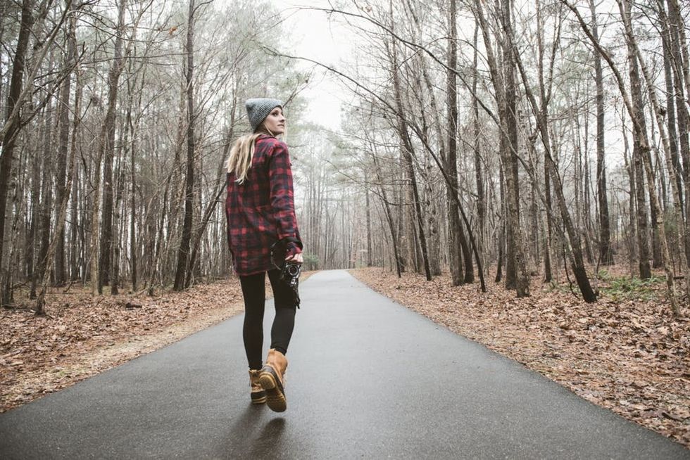 A woman walks down a rural road holding a camera