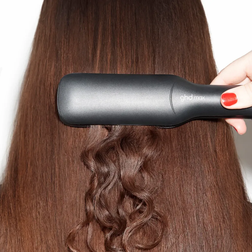a woman with curly hair using the ghd max styler to straighten her hair