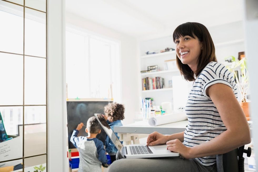 A woman works on a laptop while children play