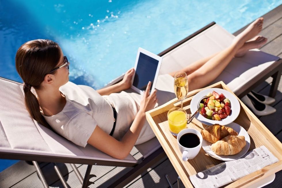 A woman works on a tablet as she eats breakfast by a pool