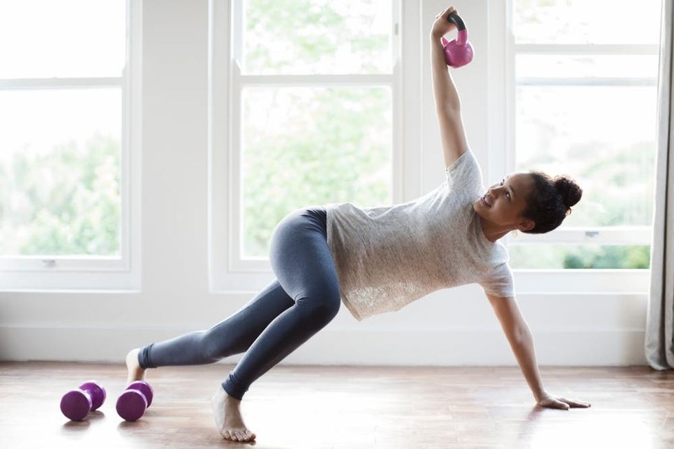 A woman works out with kettlebells in a sunny room