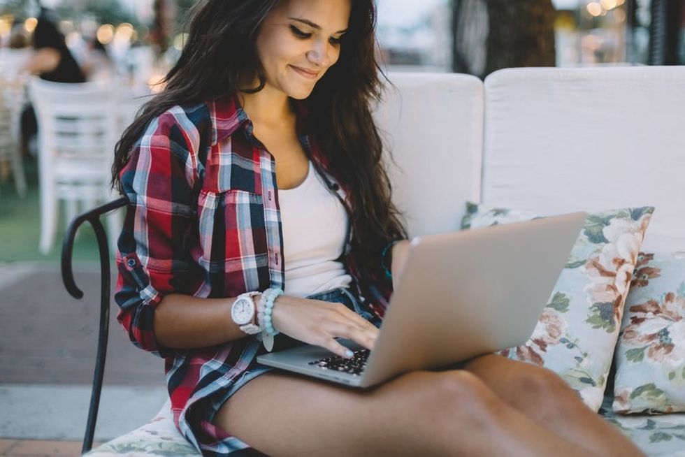 A woman works sitting on a bench outside at a cafe