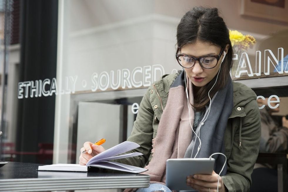 A woman writes in a journal while looking at a tablet