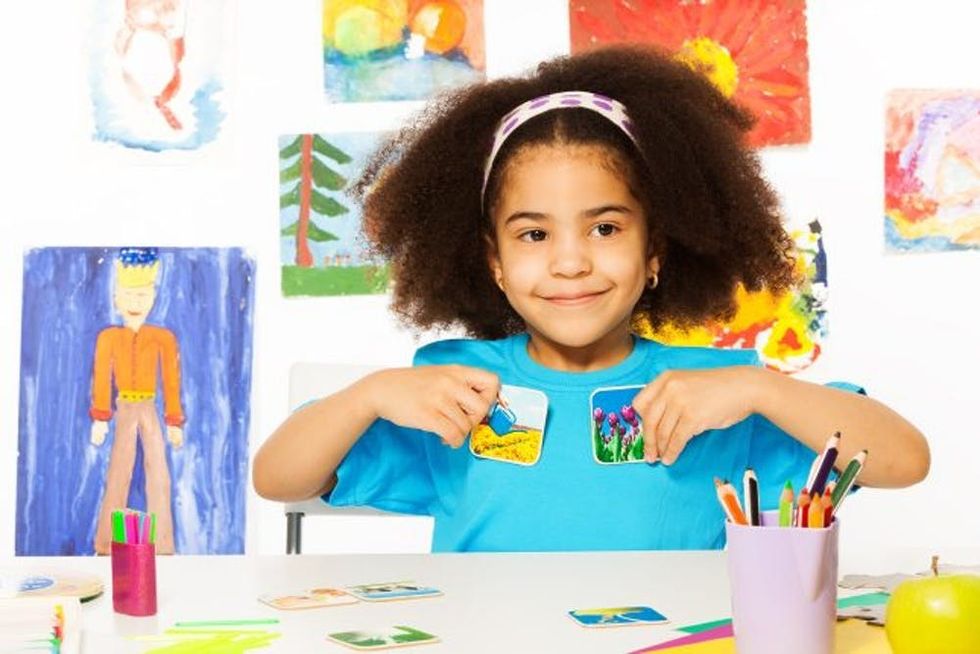 A young girl smiles and holds up flashcards