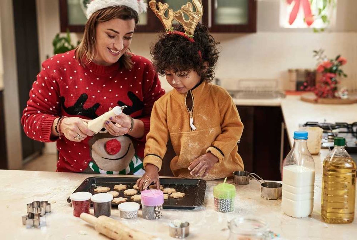 Adult and child decorating cookies together in a festive kitchen setting.
