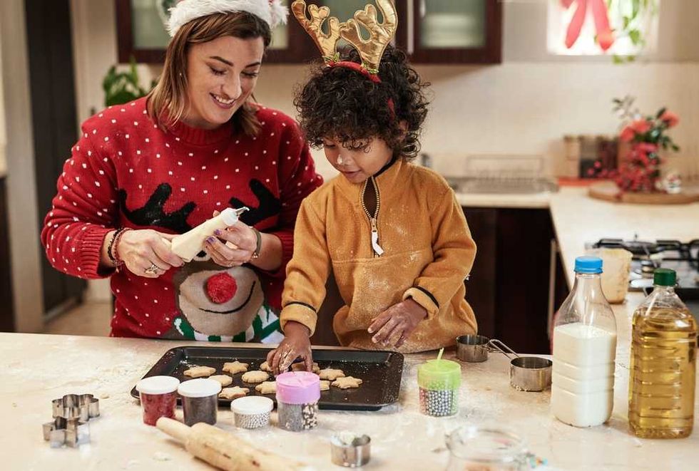 Adult and child decorating cookies together in a festive kitchen setting.