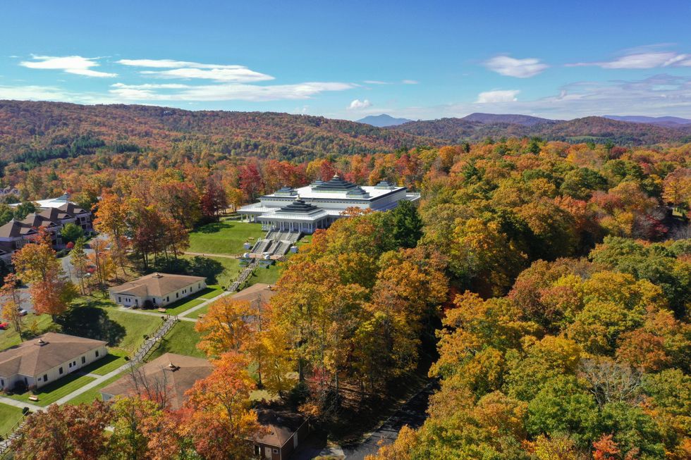 Aerial view of a building amid colorful autumn foliage with mountains in the background.