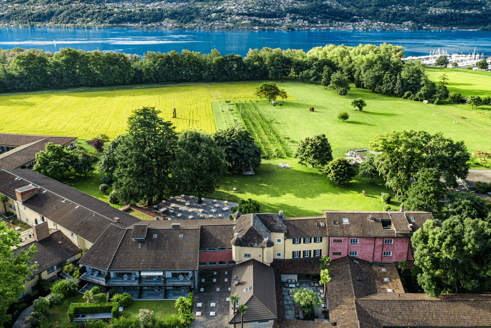 Aerial view of a countryside estate by a serene lake with lush green fields and trees.