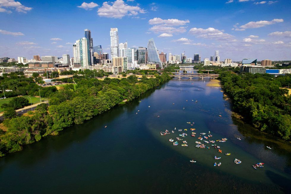 Aerial view of a river with kayakers, city skyline, and green shorelines.