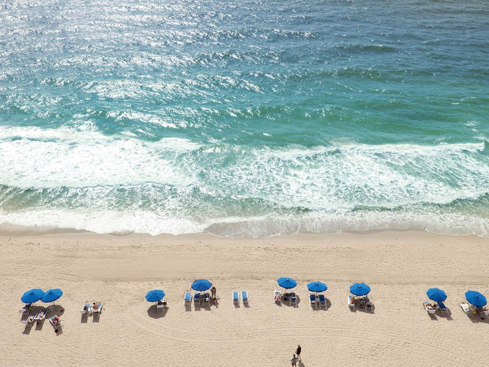 Aerial view of beach with blue umbrellas and ocean waves.