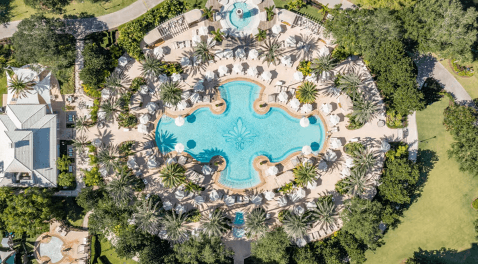Aerial view of resort pool with loungers, umbrellas, and surrounding greenery.