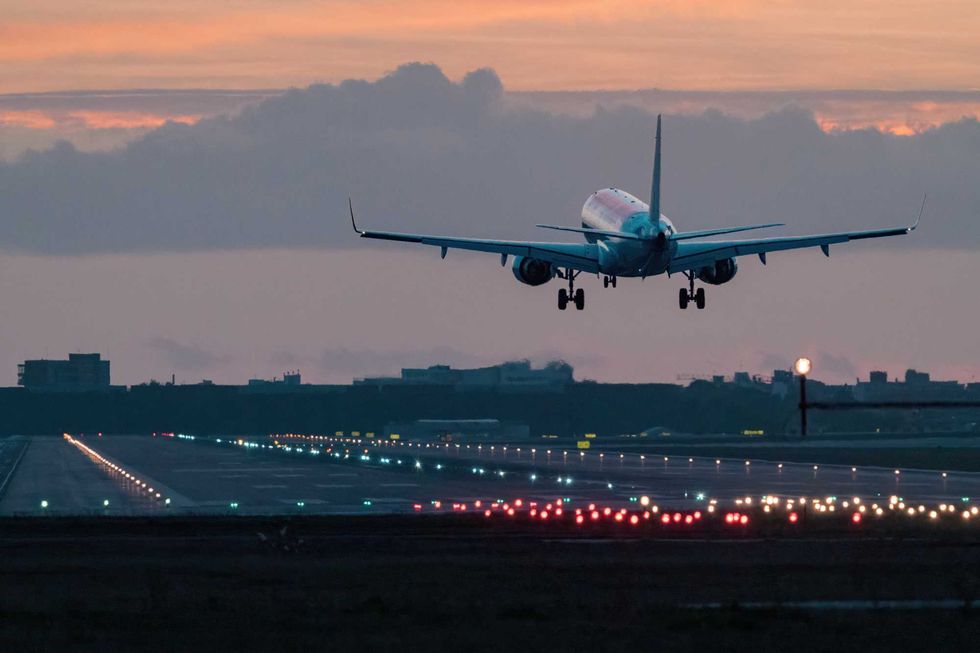 Airplane landing on runway at sunset with city skyline in background.