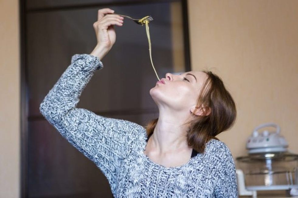 Amusing attractive young woman eating pasta in kitchen