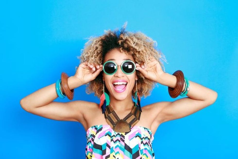 An excited, stylish young woman adjusts her sunglasses