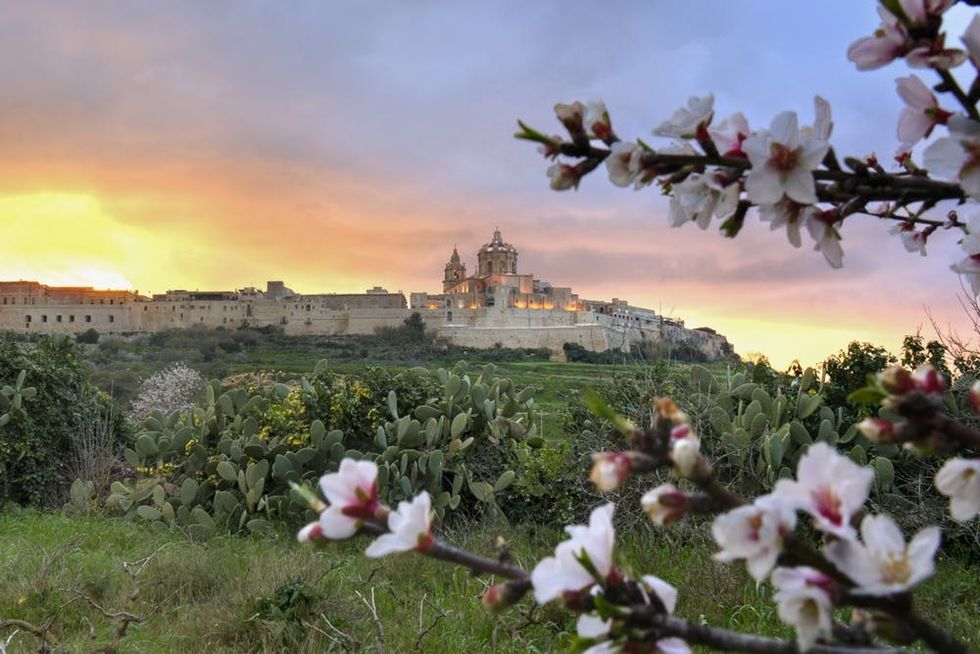 An orange sunset hovers over the ancient city of Mdina