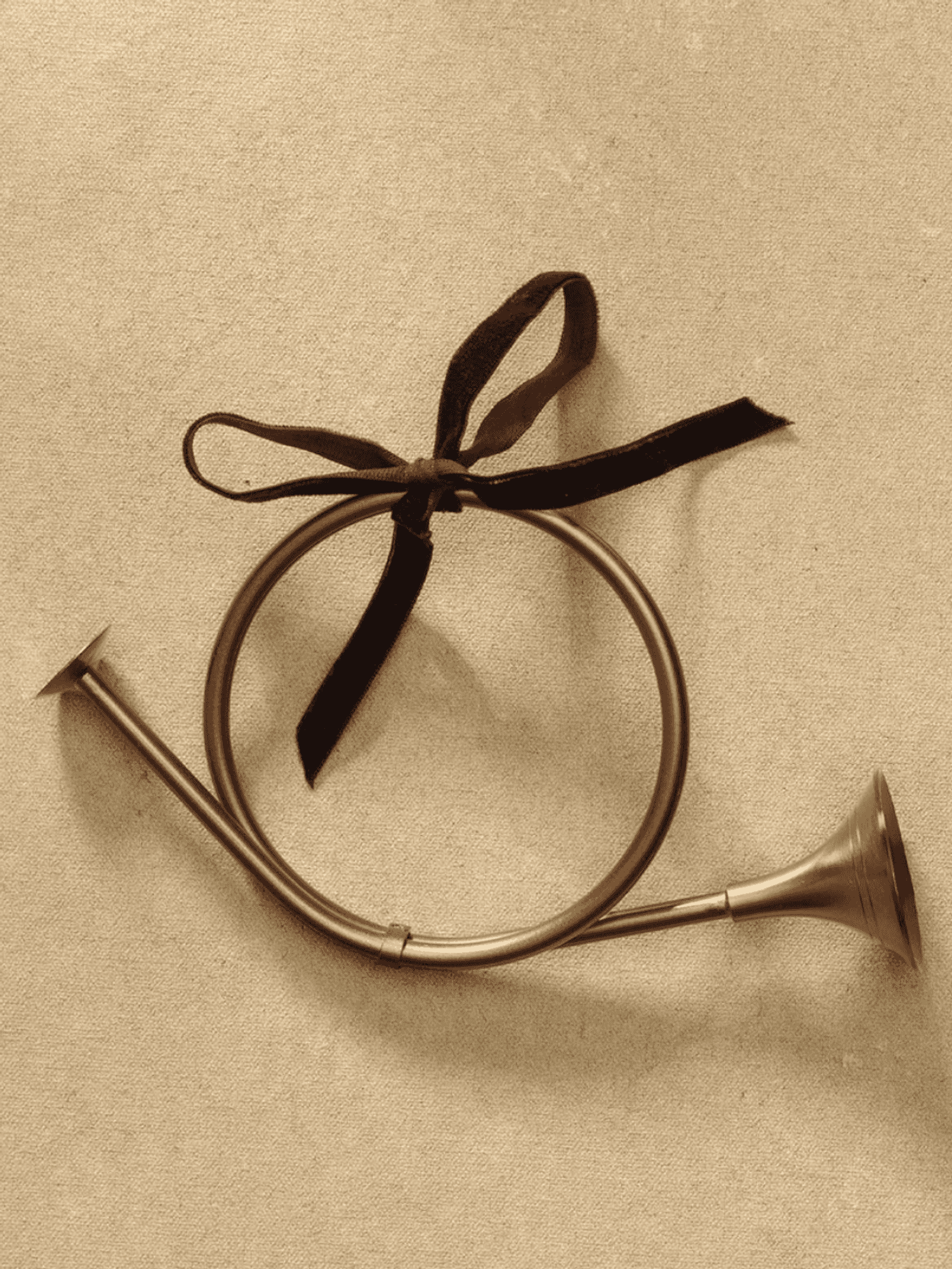 Antique brass horn with a black ribbon, set against a textured, beige background.