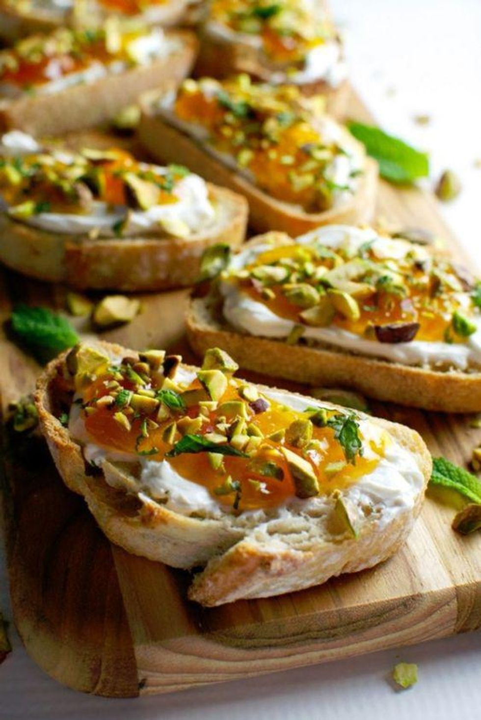 apricot and goat cheese with pistachio pieces and mint on a wood cutting board Summer Crostini Recipes