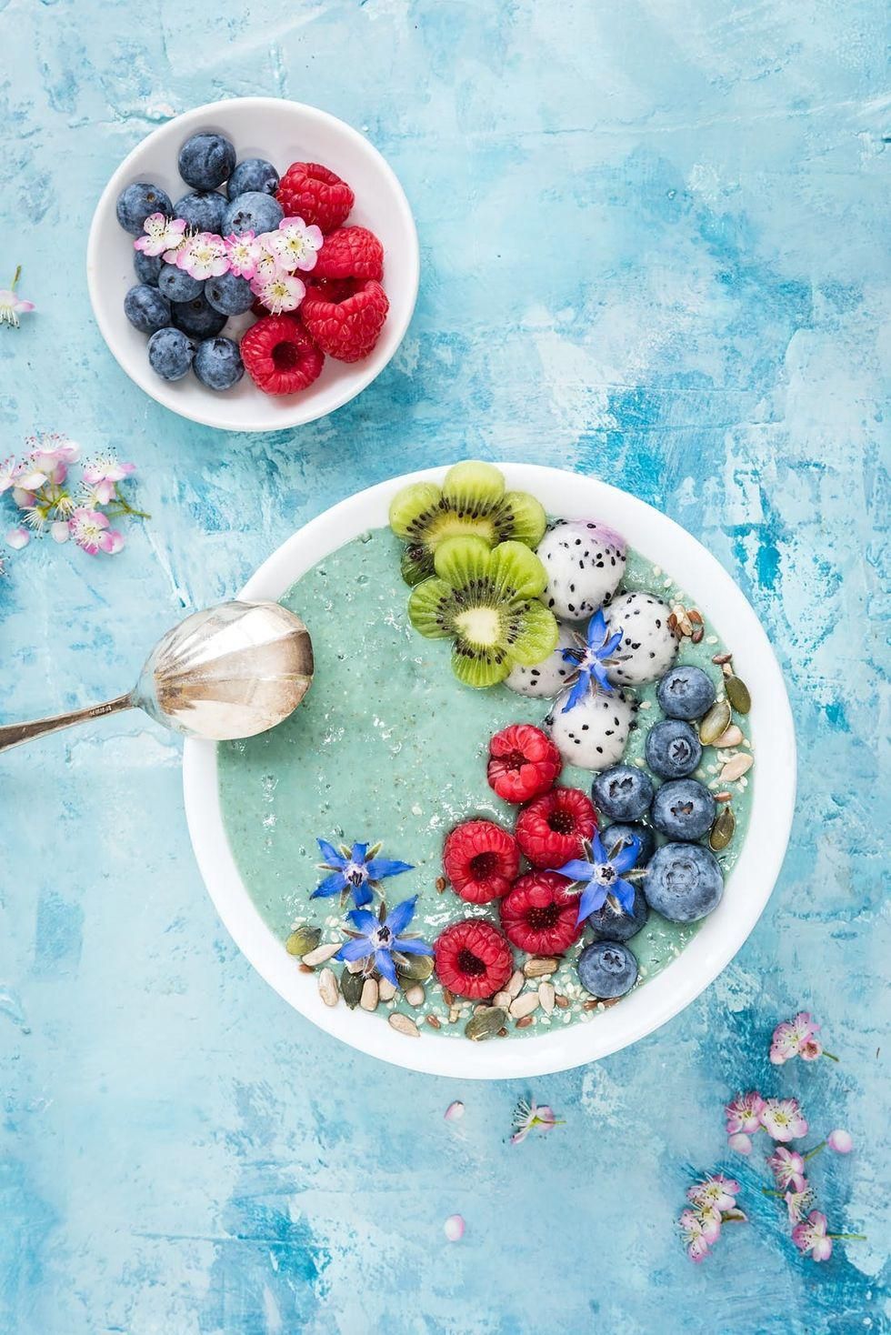 aqua colored mermaid smoothie bowl with berries, nuts, and flowers