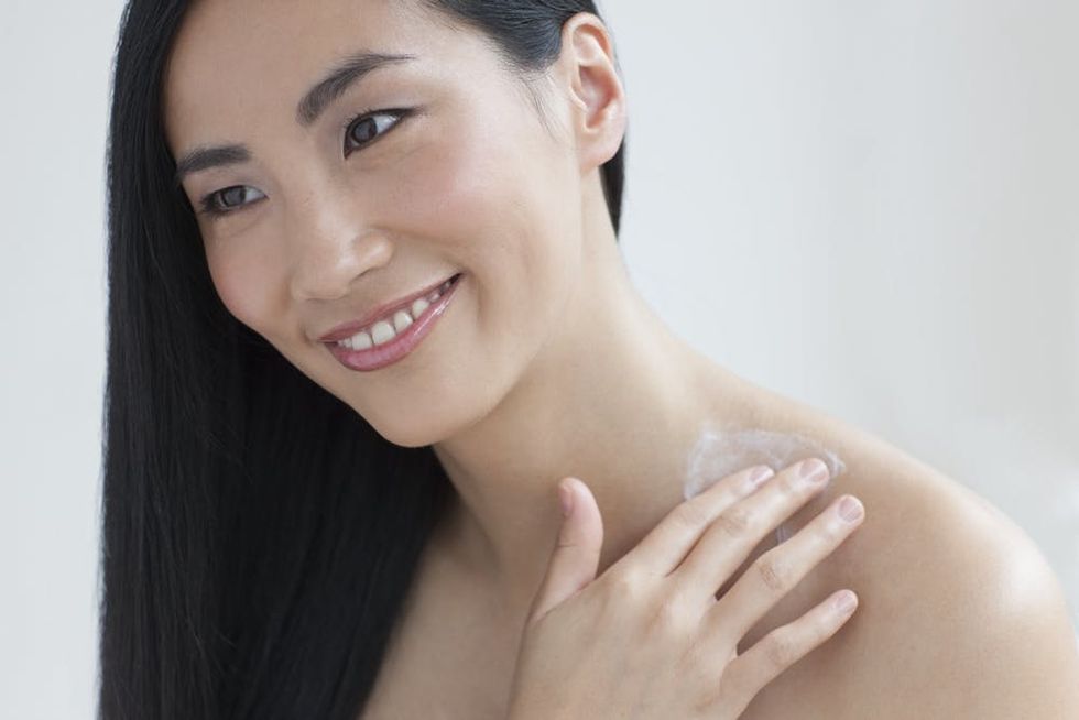 Asian woman applying cream to her neck. 