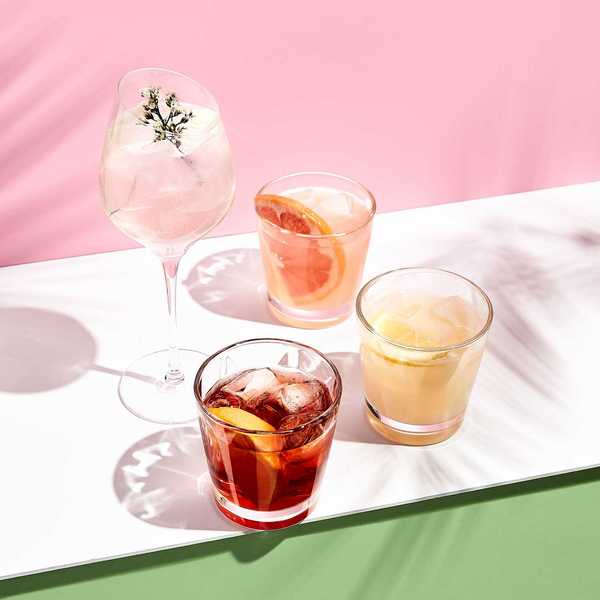 Assorted cocktails with citrus and herbs on a pink and green background.