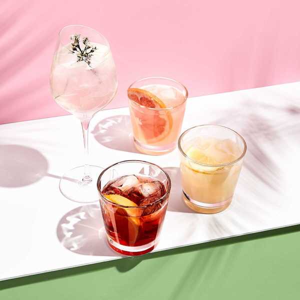 Assorted cocktails with citrus and herbs on a pink and green background.