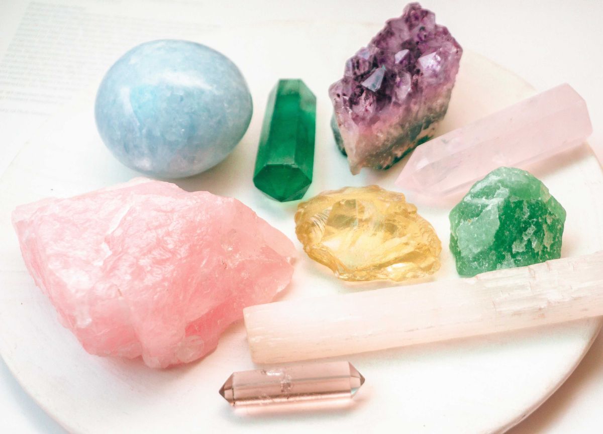Assorted colorful crystals on a white plate, including rose, blue, and green hues.