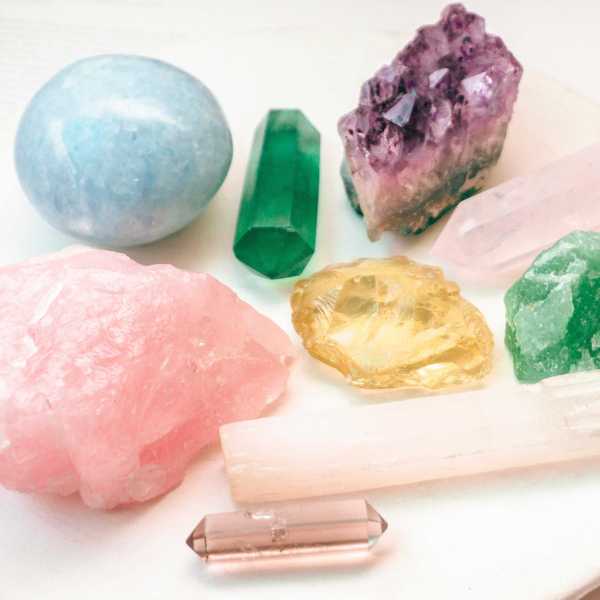 Assorted colorful crystals on a white plate, including rose, blue, and green hues.