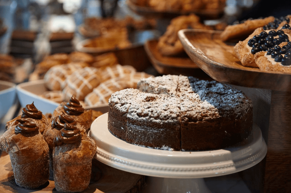 Assorted pastries including a sliced cake, muffins, and tarts with blueberries on display.