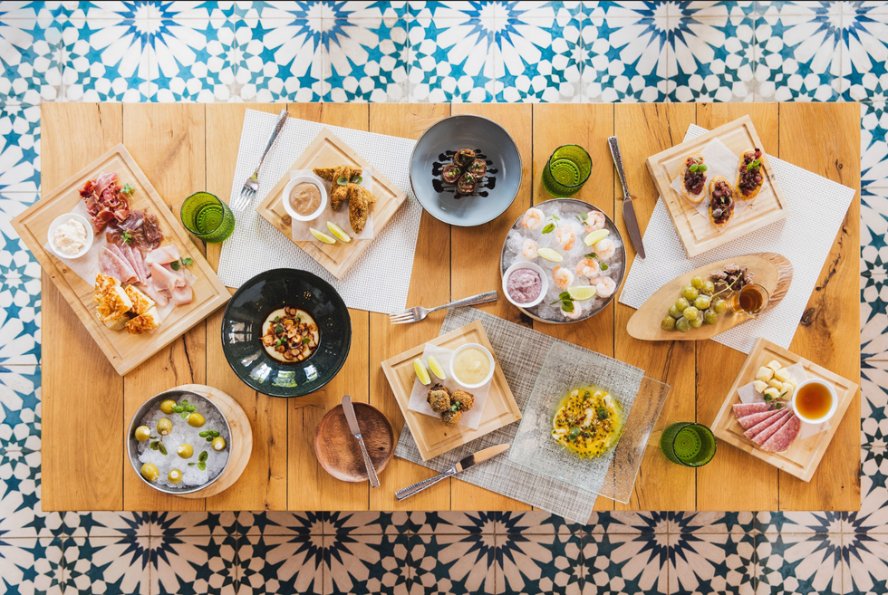 Assorted tapas on a wooden table with decorative tiled floor background.