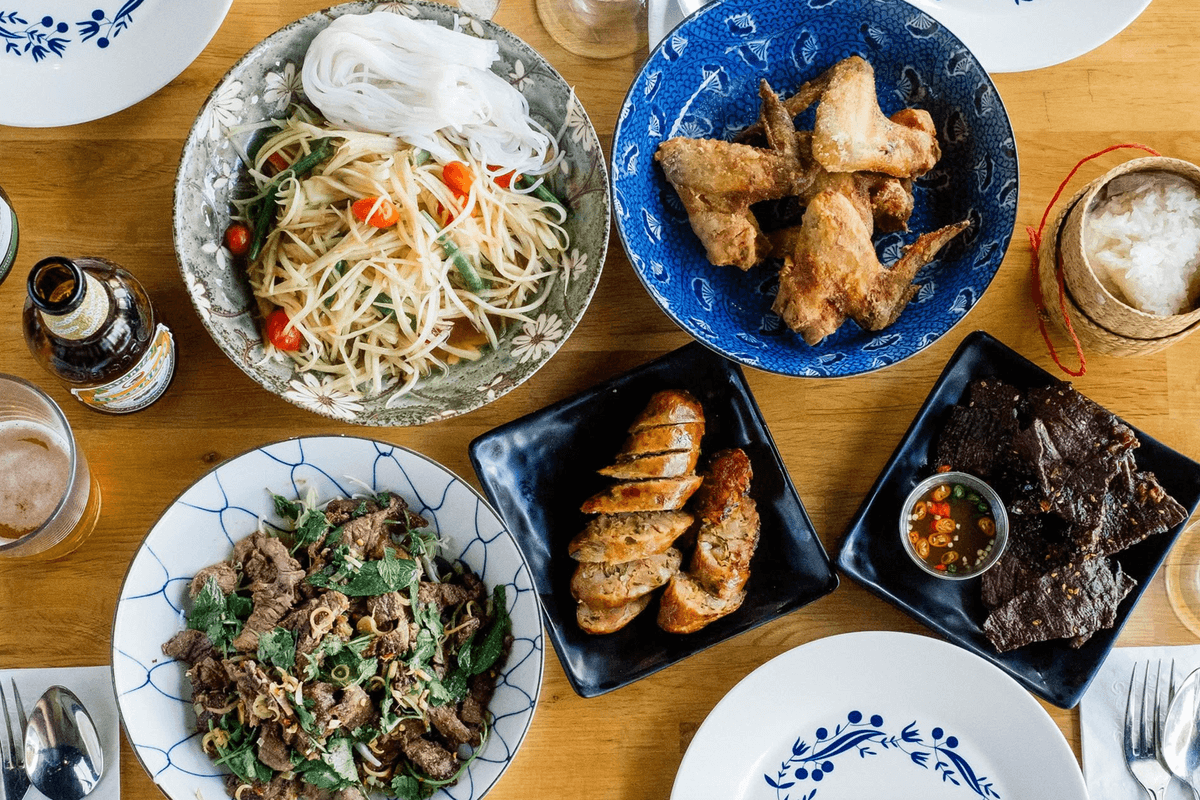Assorted Thai dishes on a table, including noodles, salads, meats, and drinks.