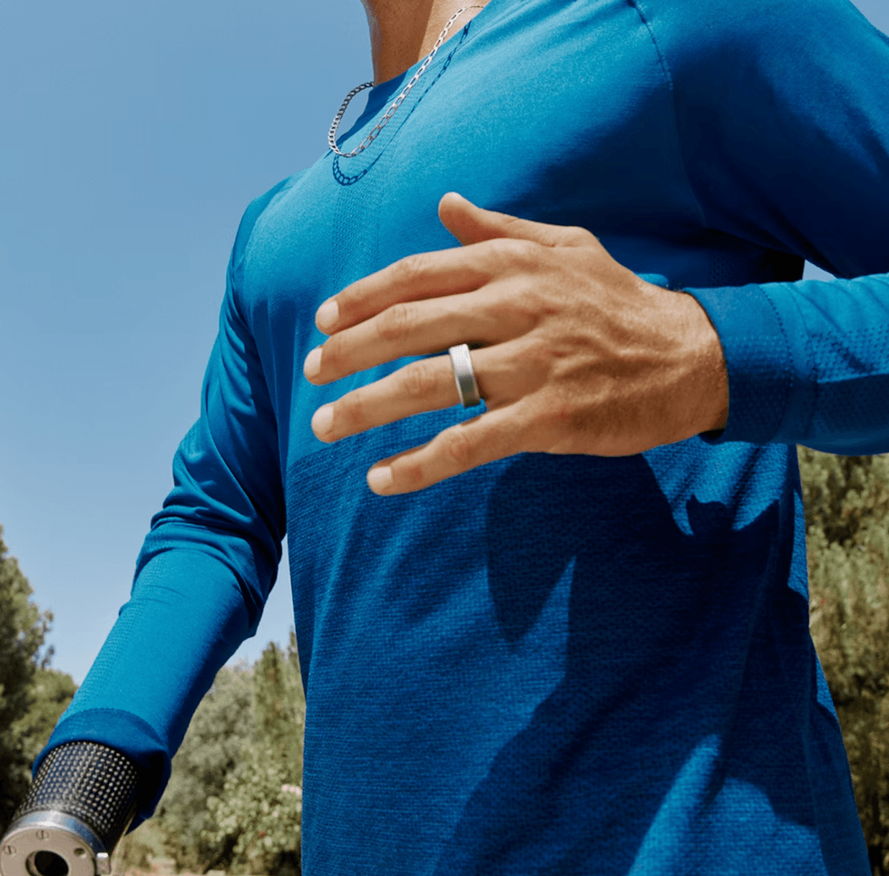 Athlete running with a prosthetic arm, wearing a blue shirt and ring, under clear skies.