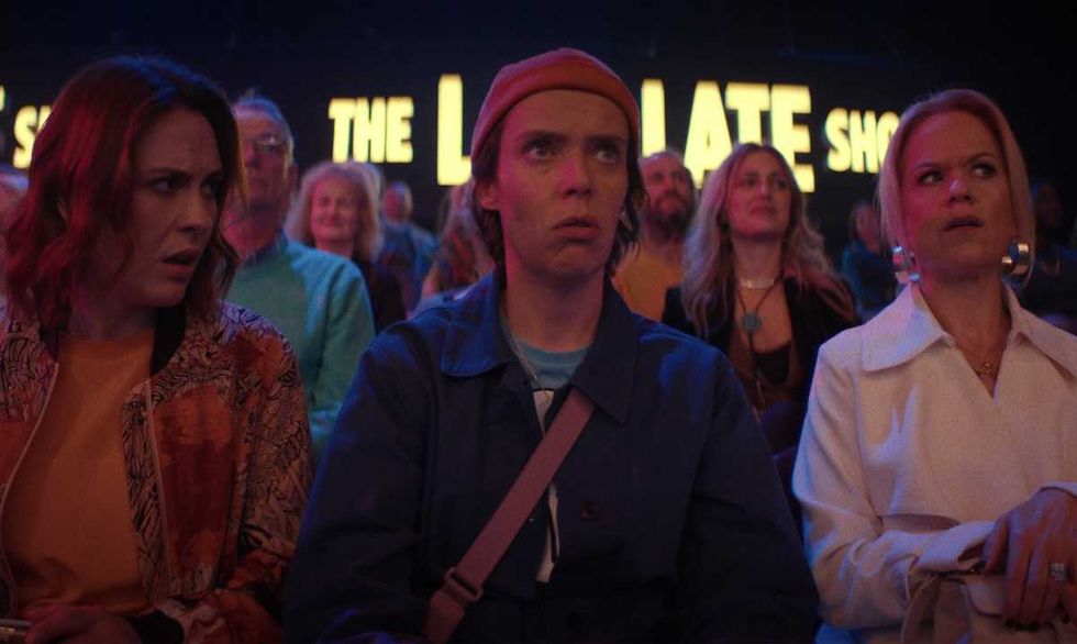 Audience looking surprised at a show with bright signs in the background.