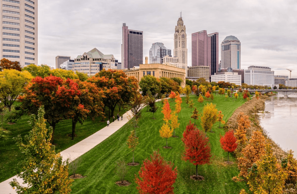 Autumn city skyline with colorful trees along a riverside park path.
