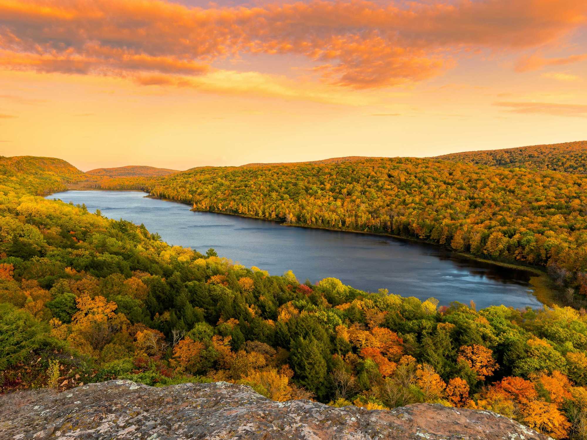 Autumn landscape with a winding river and vibrant fall foliage under an orange sky.