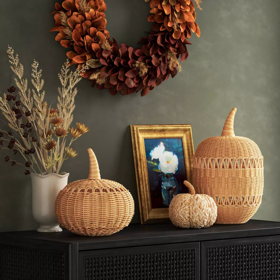 Autumn wreath, vase, wicker pumpkins, and framed art on a black cabinet.