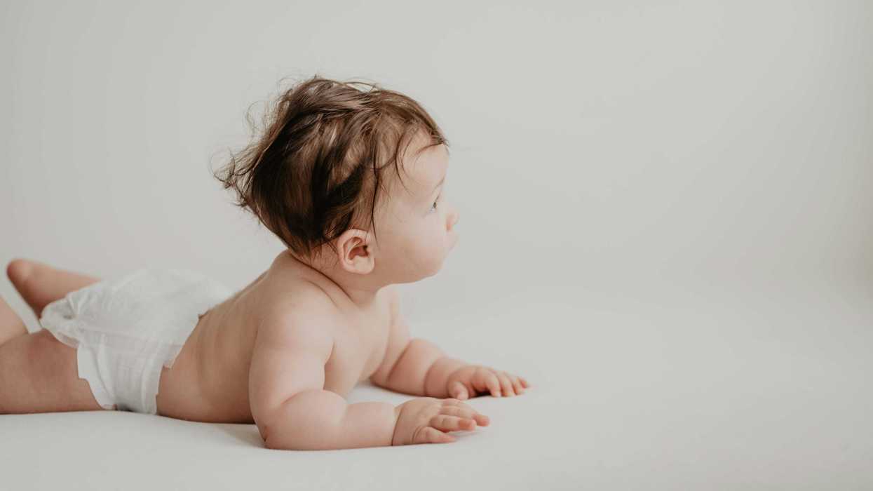 Baby in a diaper lying on stomach looking to the side, on a white background.