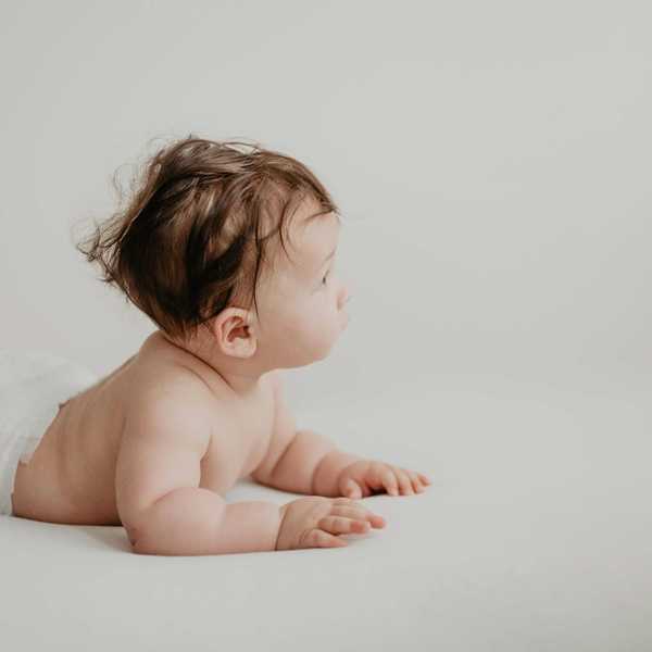 Baby in a diaper lying on stomach looking to the side, on a white background.