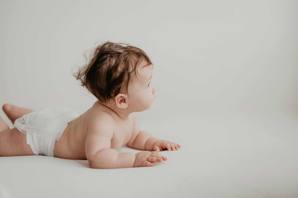 Baby in a diaper lying on stomach looking to the side, on a white background.