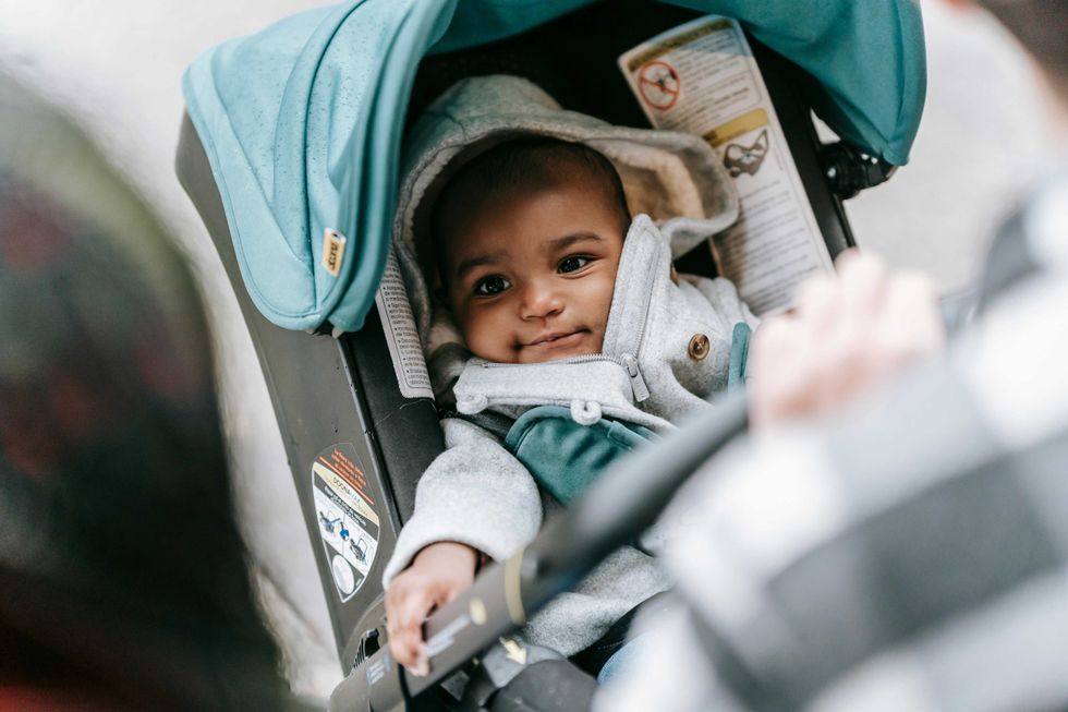 Baby in a stroller smiles, wearing a hooded coat with a green canopy overhead.