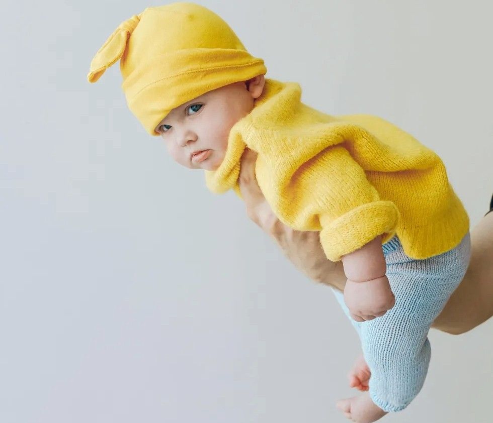 baby in a yellow sweater being held