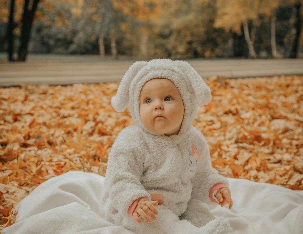 Baby in bunny suit sitting on a blanket in autumn leaves.
