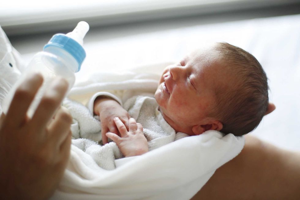Baby in white blanket, smiling, with a bottle near.