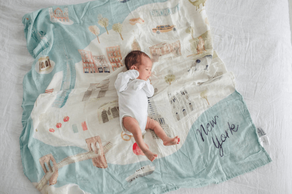 Baby on New York-themed blanket, peacefully sleeping in white outfit.