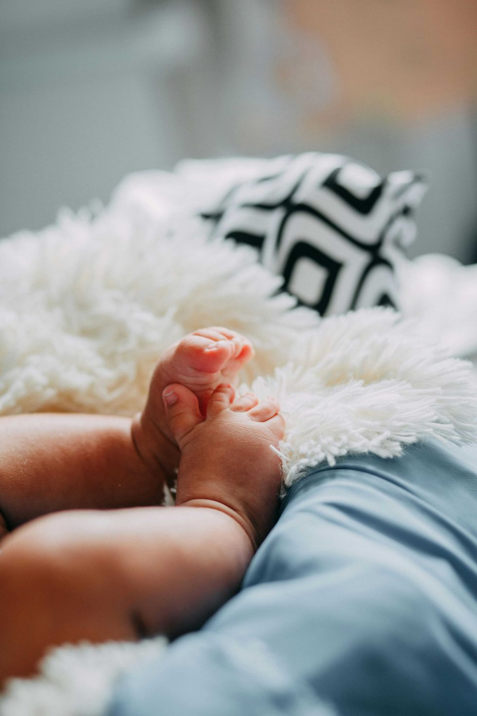 Baby's feet on a fluffy white blanket with a patterned pillow in the background.